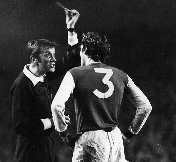 1976: During a match between London football clubs Arsenal and Chelsea, Arsenal player Sammy Nelson is booked by referee Ray Toseland, who holds up...