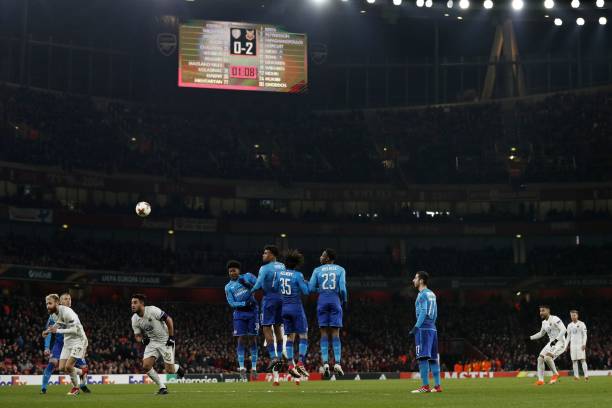 The scoreboard shows the 0-2 scoreline as Ostersunds' Iranian striker Saman Ghoddos (2nd R) takes a freekick during the second leg of the Europa League Round of 32 football match between Arsenal and Ostersunds at the Emirates Stadium in London on February 22, 2018. / AFP PHOTO / Adrian DENNIS / 