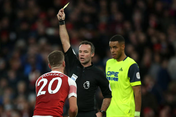 English referee Paul Tierney shows a yellow card to Arsenal's German defender Shkodran Mustafi (L) for simulation during the English Premier League...