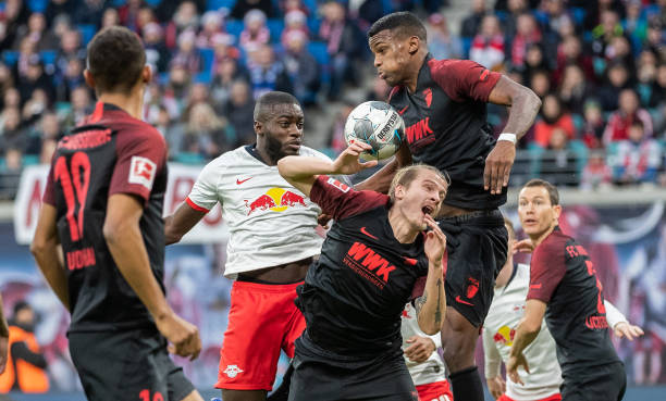 LEIPZIG, GERMANY - DECEMBER 21: Dayot Upamecano of RB Leipzig jumps for a header with Tin Jedvaj and Sergio Cordova of FC Augsburg during the Bunde...