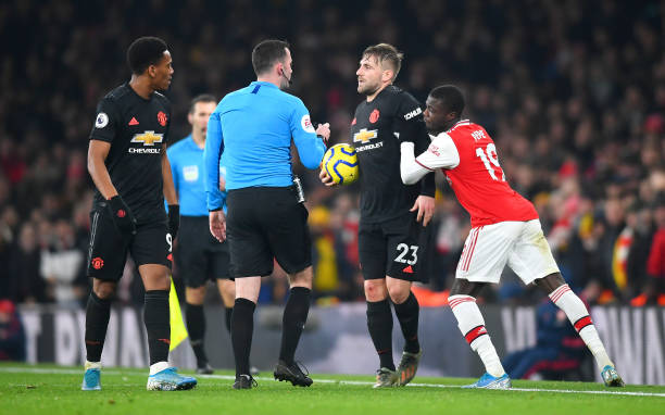 LONDON, ENGLAND - JANUARY 01: Nicolas Pepe of Arsenal pushes Luke Shaw of Manchester United as referee Chris Kavanagh speaks to them both during the Premier League match between Arsenal FC and Manchester United at Emirates Stadium on January 01, 2020 in London, United Kingdom. (Photo by Clive Mason/Getty Images)