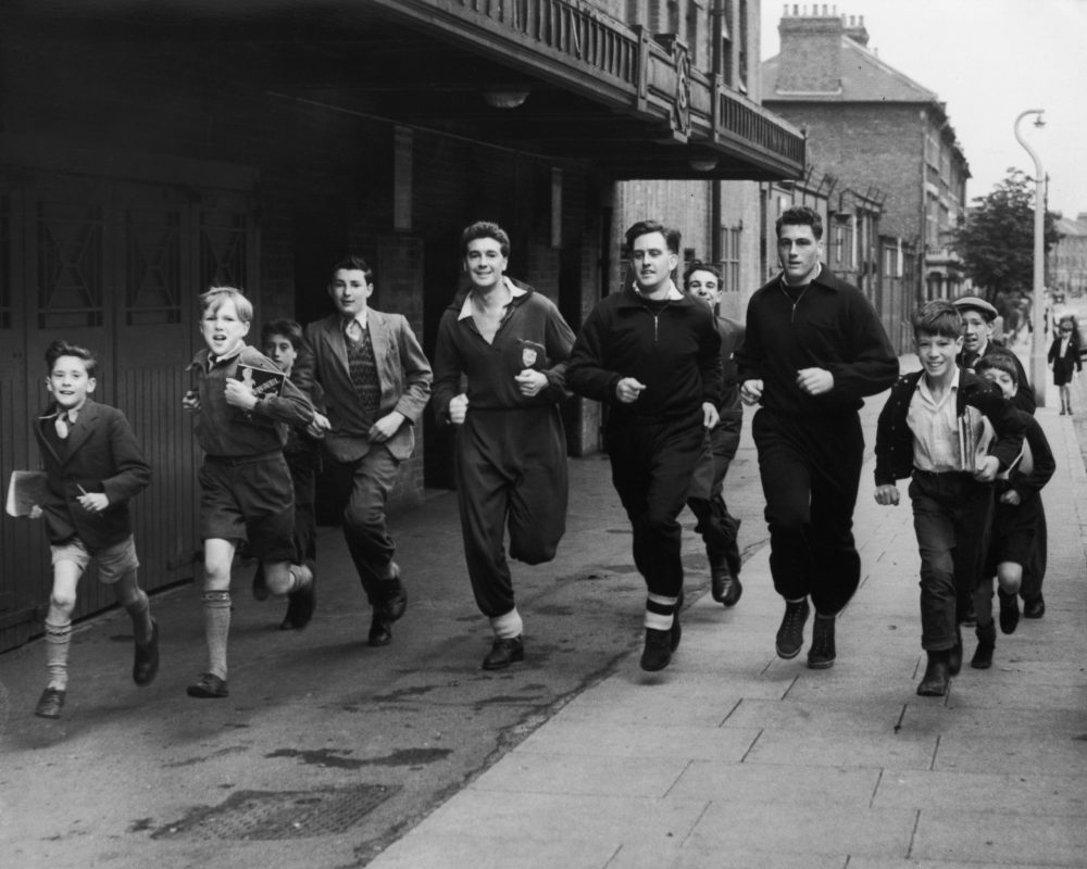 13 August, 1950: Arsenal forward jokes he's been sold to Korea United 3 The schoolboy fans have fun running in the streets around Highbury Stadium with members of the Arsenal football team, (left to right), Wilkins, David Bowen and Cliff Holton, 25th July 1954. (Photo by William Vanderson/Fox Photos/Hulton Archive/Getty Images)