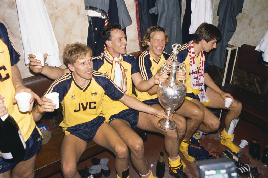 LIVERPOOL, UNITED KINGDOM - MAY 26: Arsenal players from left Kevin Richardson, Steve Bould, Paul Merson and Alan Smith celebrate in the dressing room with the League Division One trophy after Arsenal had beaten Liverpool 2-0 in the final game of the season to pip Liverpool to the title, at Anfield on May 26, 1989 in Liverpool, England. (Photo by Allsport/Getty Images)