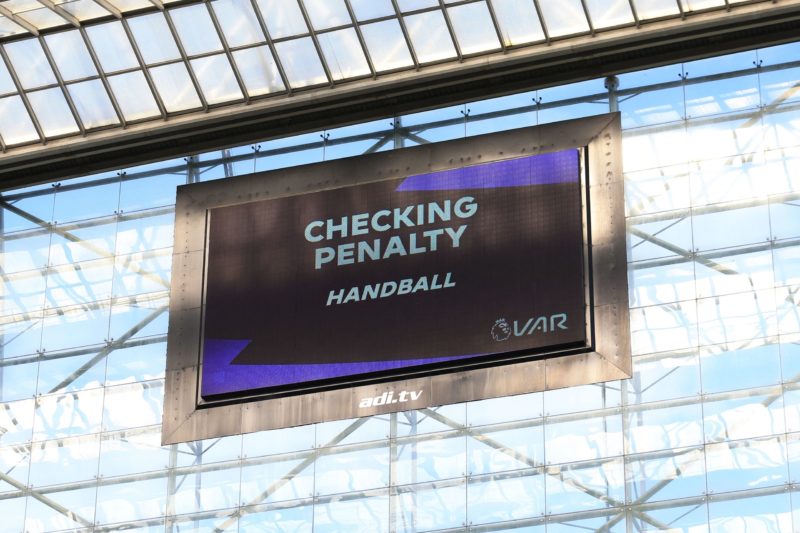 The big screen shows the VAR (Video Assistant Referee) action, checking for a penalty for handball during the English Premier League football match...