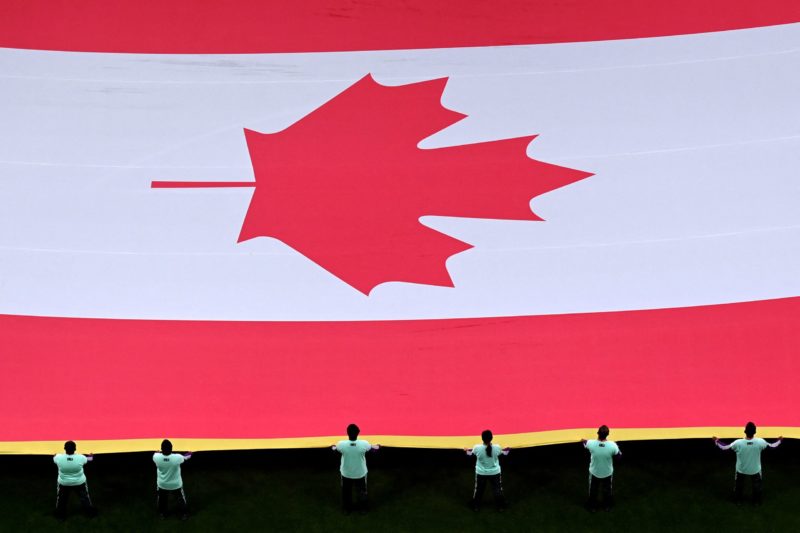 TOPSHOT - Volunteers hold Canada's flag ahead of the Qatar 2022 World Cup Group F football match between Belgium and Canada at the Ahmad Bin Ali St...