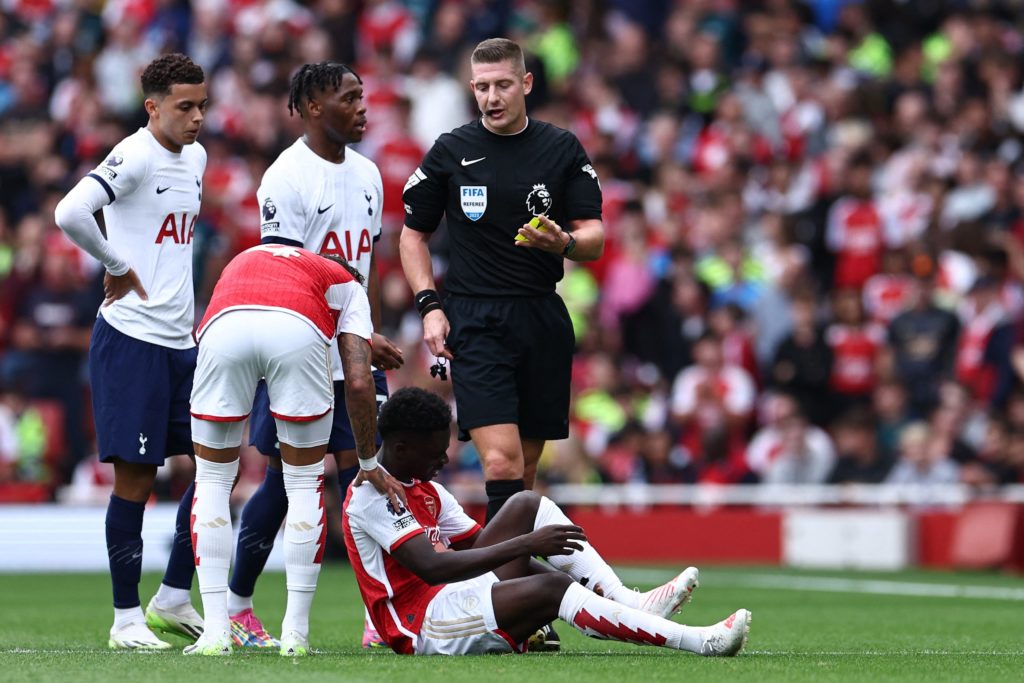 Bukayo Saka injury latest after knock left him in severe pain 2 English referee Robert Jones (C) books Tottenham Hotspur's Italian defender #38 Destiny Udogie (3L) after a foul on Arsenal's English midfielder #07 Bukayo Saka during the English Premier League football match between Arsenal and Tottenham Hotspur at the Emirates Stadium in London on September 24, 2023. (Photo by HENRY NICHOLLS/AFP via Getty Images)