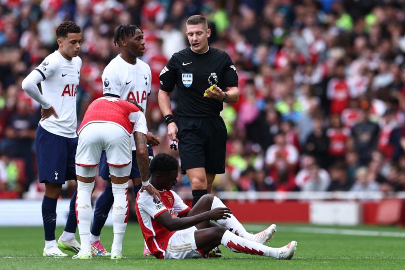 English referee Robert Jones (C) books Tottenham Hotspur's Italian defender #38 Destiny Udogie (3L) after a foul on Arsenal's English midfielder #07 Bukayo Saka during the English Premier League football match between Arsenal and Tottenham Hotspur at the Emirates Stadium in London on September 24, 2023. (Photo by HENRY NICHOLLS/AFP via Getty Images)