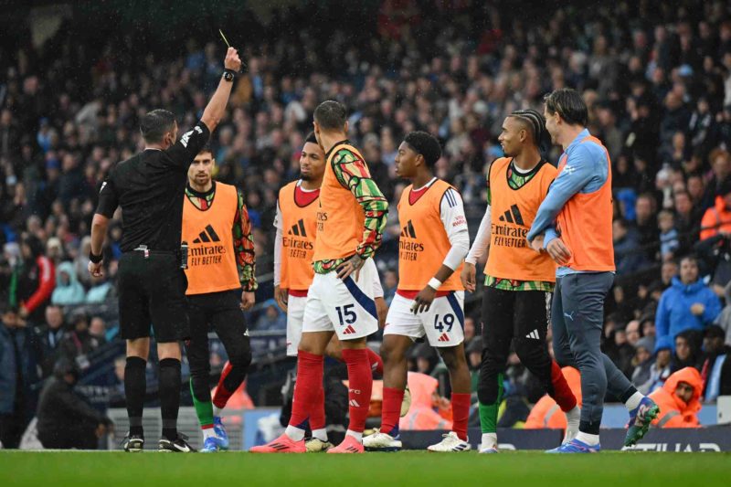 MANCHESTER, ENGLAND - SEPTEMBER 22: Referee, Michael Oliver shows a yellow card to Myles Lewis-Skelly of Arsenal during the Premier League match be...