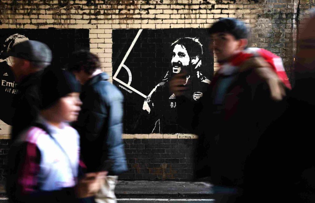 LONDON, ENGLAND - DECEMBER 14: Fans walk past a mural featuring Arsenal set piece coach Nicolas Jover prior to the Premier League match between Arsenal FC and Everton FC at Emirates Stadium on December 14, 2024 in London, England. (Photo by Alex Pantling/Getty Images)