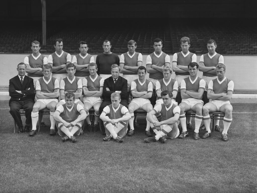 The Arsenal players ((back) Northern Irish footballer Eddie Magill, British footballer Eddie Clamp (1934-1995), British footballer Vic Groves (1932-2015), British footballer Jack Kelsey (1929-1992), Northern Irish footballer Billy McCullough, British footballer John Snedden, British footballer Laurie Brown (1937-1998), Northern Irish footballer Terry Neill (1942-2022), (middle) British football coach and former footballer Bertie Mee (1918-2001), British footballer John Barnwell, British footballer Geoff Strong (1937-2013), British footballer George Eastham, British football manager and former footballer Billy Wright (1924-1994), British footballer Johnny MacLeod, British footballer John Petts, British footballer Alan Skirton (1939-2019), British footballer Dave Bacuzzi (1940-2020), (on ground) British footballer Joe Baker (1940-2003), British footballer Arfon Griffiths, and British footballer Gerry Ward (1936-1994)) pose for a team portrait ahead of the 1962/63 English League Division One season, at the club's Highbury ground in London, England, 8th August 1962. (Photo by Evening Standard/Hulton Archive/Getty Images)