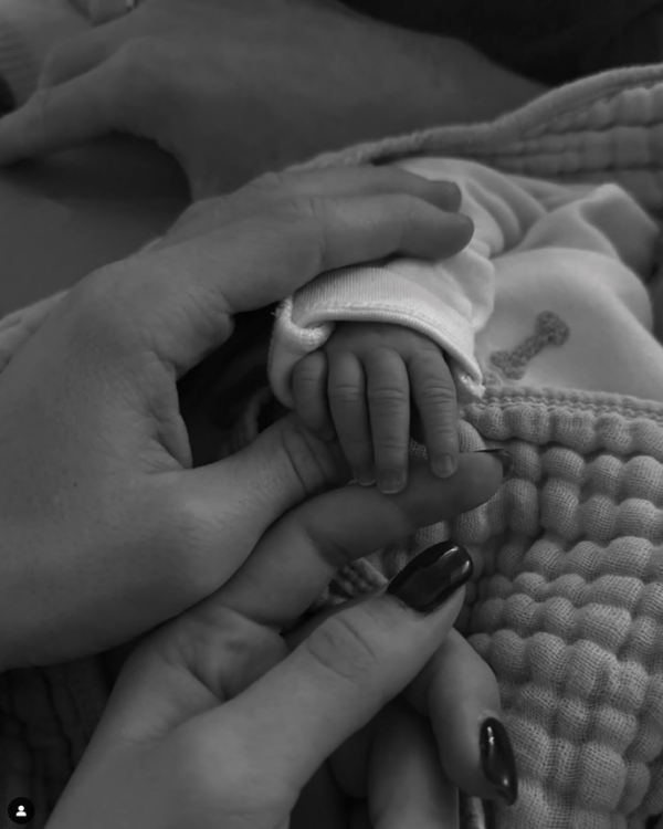 Black-and-white image of Martin Ødegaard and Helene Spilling holding their newborn baby boy's tiny hand, wrapped in a soft blanket.