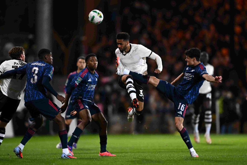 George Hall of Port Vale headers the ball whilst under pressure from Cristhian Mosquera, Myles Lewis-Skelly and Christian Noergaard of Arsenal duri...