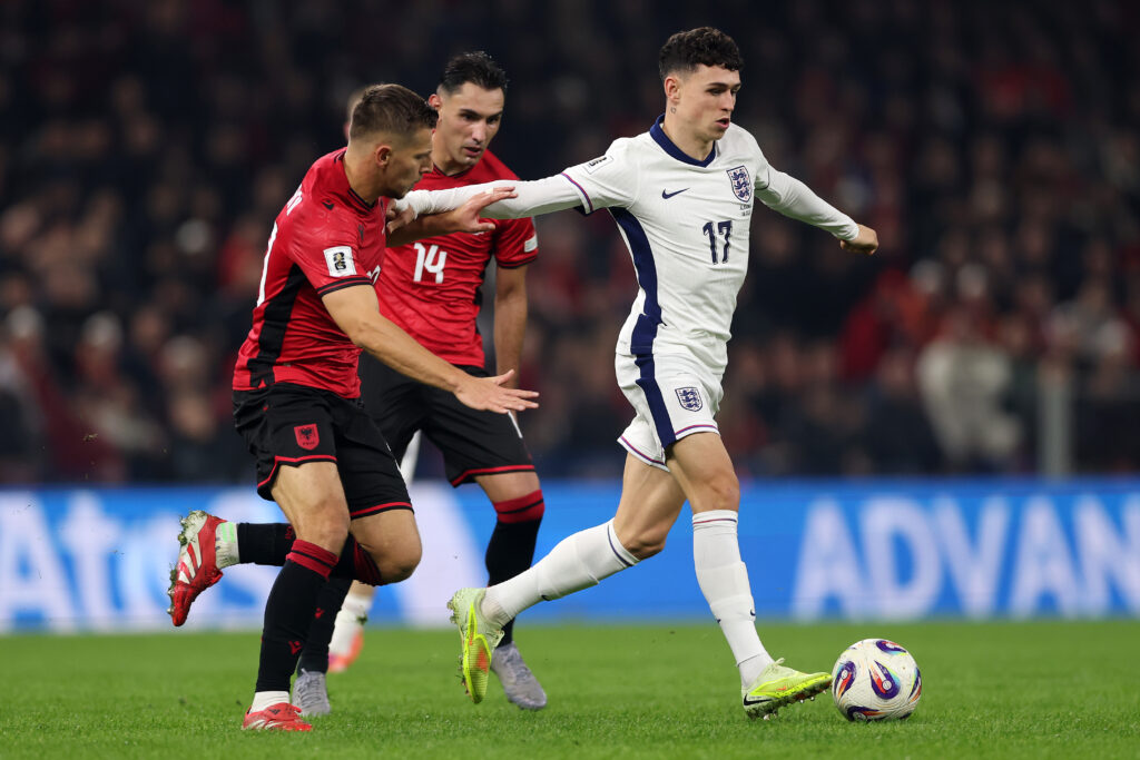TIRANA, ALBANIA - NOVEMBER 16: Phil Foden of England runs with the ball past Qazim Laci and Ylber Ramadani of Albania during the FIFA World Cup 2026 qualifier match between Albania and England at Air Albania Stadium on November 16, 2025 in Tirana, Albania. (Photo by Alex Pantling/Getty Images)