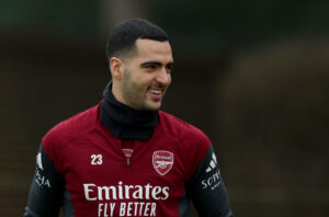 Mikel Merino, wearing a deep red Arsenal training top, smiles as he looks to his right
