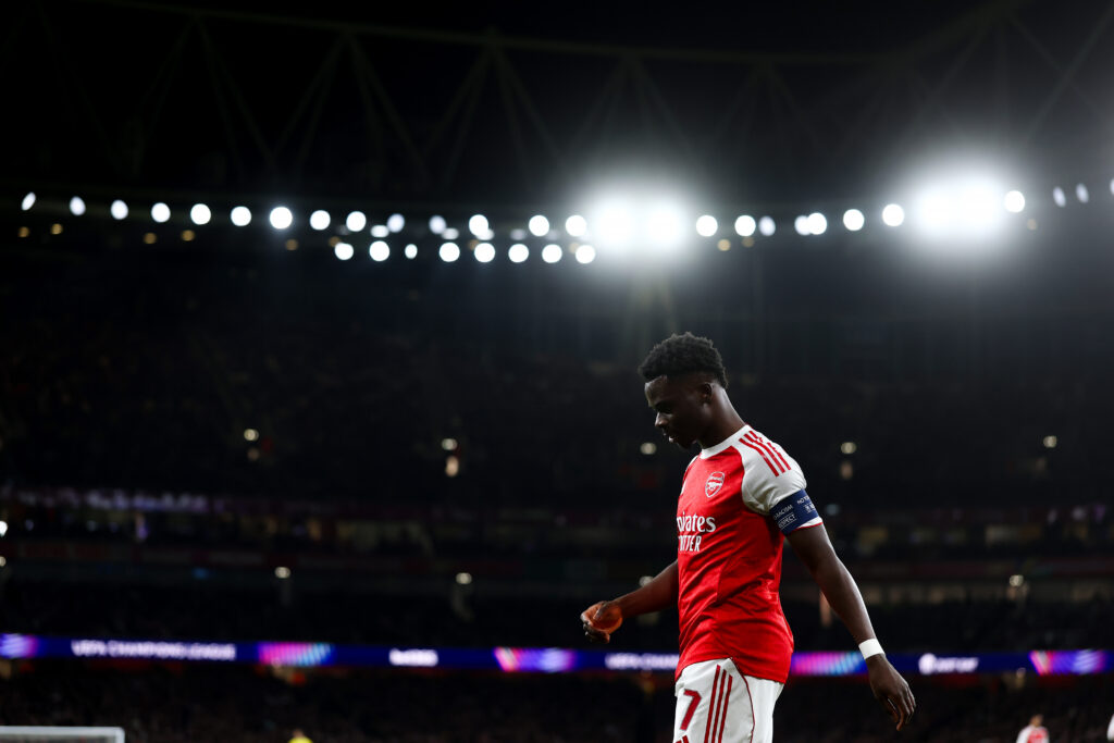 Bukayo Saka framed against a black night and the Emirates Stadium lights