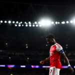Bukayo Saka framed against a black night and the Emirates Stadium lights