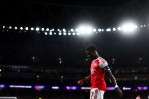 Bukayo Saka framed against a black night and the Emirates Stadium lights