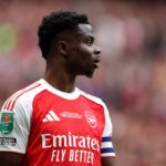 Bukayo Saka in a home Arsenal kit, looking to the side