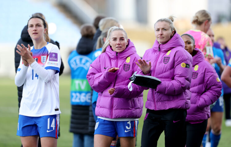 Leah Williamson, wearing a pink puffer jacket, applauds England fans as she stands beside Greenwood and Wubben-Moy