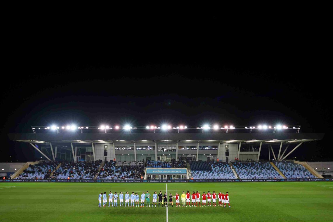 Arsenal u21s lineup at Manchester City's Joie Stadium in front of a half empty stand at night