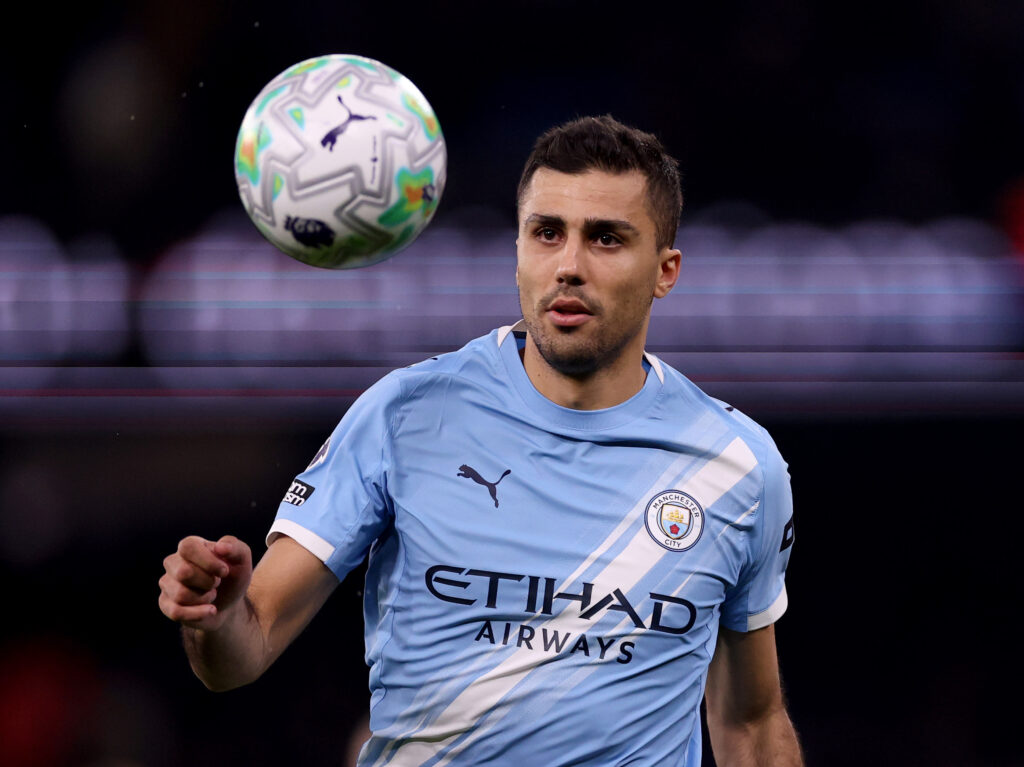 Rodri watches the ball closely during a Manchester City match, in a close-up action shot with the ball suspended in front of him.