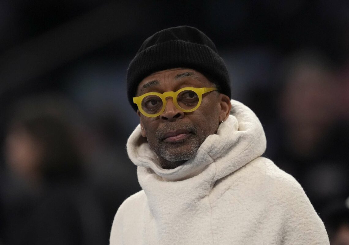 Spike Lee wearing round glasses, a beanie hat and a large white fleece jumper with a hood