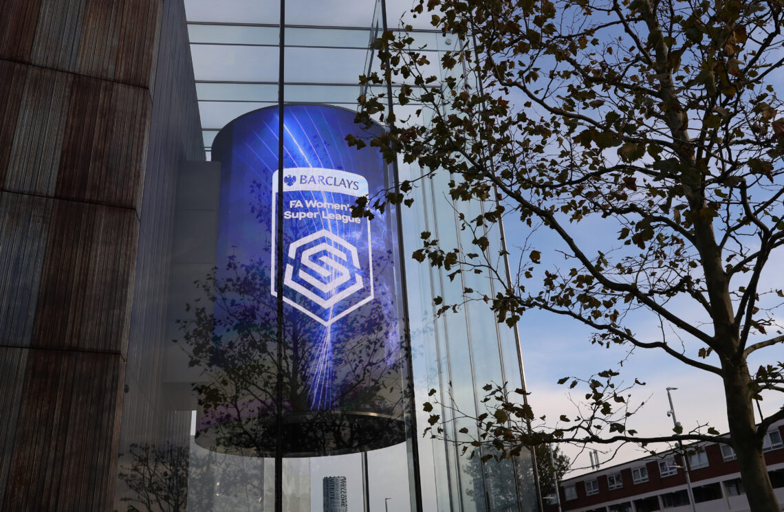 Large curved digital screen on the exterior of a modern glass building displaying the Barclays FA Women’s Super League logo, with bare tree branche...