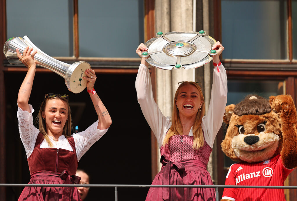 Georgia Stanway of FC Bayern Munich holds the DFB Pokal trophy and Magdalena Eriksson of FC Bayern Munich holds the Bundesliga Meisterschale as they greet their fans at Marienplatz during the official championships celebration