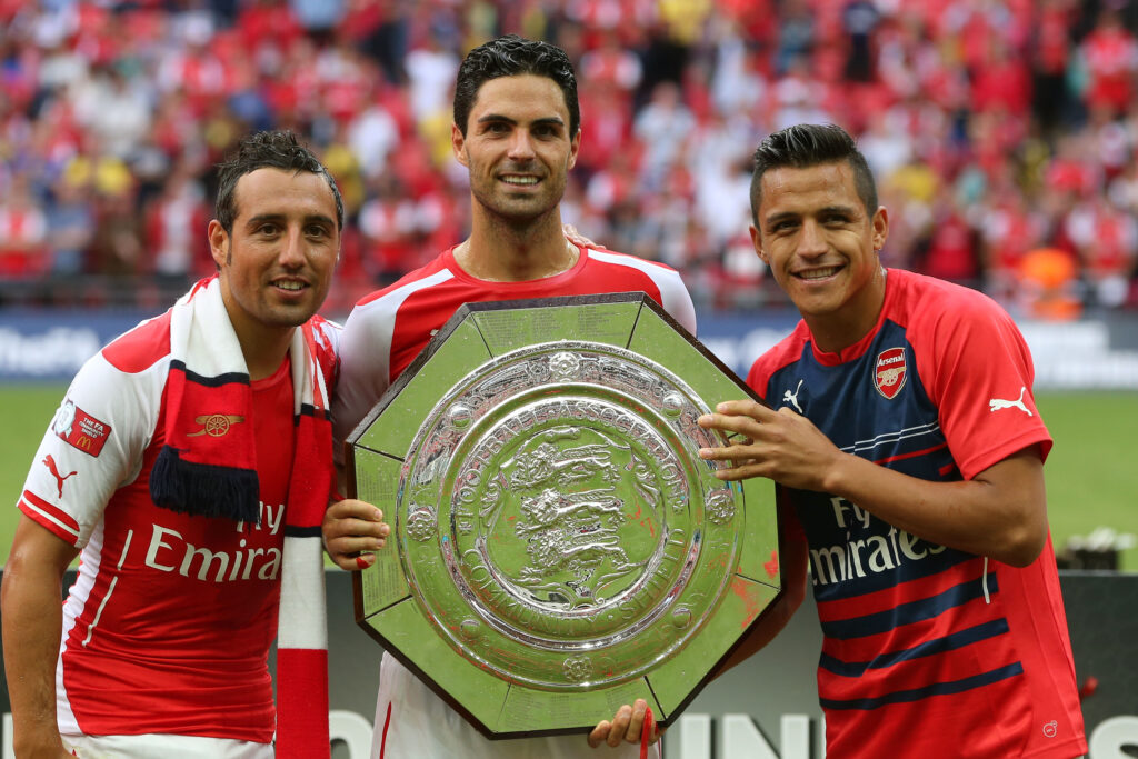 Mikel Arteta of Arsenal holds up the trophy next to Santi Cazorla (L) and Alexis Sanchez after the FA Community Shield match between Manchester City and Arsenal at Wembley