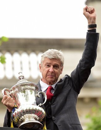 Arsenal's French manager Arsene Wenger holds the trophy from the top deck of an open-topped bus during the Arsenal victory parade in London on May 31, 2015, following their win in the English FA Cup final football match on May 30, 2014 against Aston Villa. Arsene Wenger's side made history at Wembley with a 4-0 rout of Aston Villa that underlined their renaissance in the second half of the campaign and served as a warning to English champions Chelsea. AFP PHOTO / LEON NEAL (Photo credit should read LEON NEAL,LEON NEAL/AFP/Getty Images)