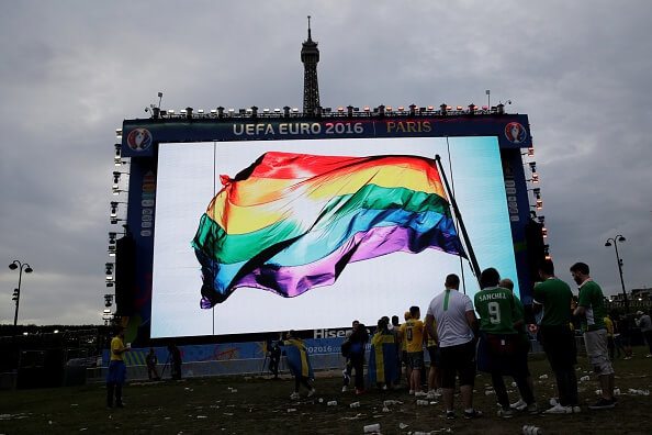 Supporters stand in front of a giant screen displaying a rainbow flag to pay tribute to the victims of the shooting of Orlando, in a fan zone in Paris during the Euro 2016 football tournament on June 13, 2016. / AFP / Thomas SAMSON (Photo credit should read THOMAS SAMSON/AFP/Getty Images)