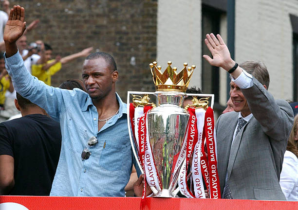 LONDON, UNITED KINGDOM: Arsenal team captain Patrick Vieira (L) and manager Arsene Wenger wave from the open-top bus carrying the winners of the British Premier League Championship, Arsenal players and their families, on its way to Islington Town Hall,16 May 2004, as part of the Club's victory celebration. (MARTYN HAYHOW/AFP/Getty Images)