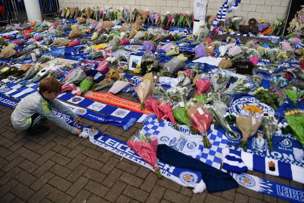 A boy arranges a club scarf around floral tributes piled outside Leicester City Football Club's King Power Stadium in Leicester, eastern England, on October 28, 2018 after a helicopter belonging to the club's Thai chairman Vichai Srivaddhanaprabha crashed outside the stadium the night before. - Leicester City's charismatic Thai chairman was the subject of growing concerns on October 28 after a helicopter belonging to the billionaire crashed and burst into flames in the stadium carpark shortly after taking off from the club's pitch following the match against West Ham United on October 27. There was no confirmation whether London-based Vichai Srivaddhanaprabha, who frequently flies to and from Leicester's home games by helicopter, was on board the aircraft which appeared to develop mechanical problems. (Photo by Ben STANSALL / AFP) (Photo credit should read BEN STANSALL/AFP/Getty Images)