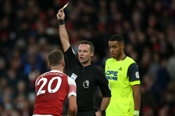 English referee Paul Tierney shows a yellow card to Arsenal's German defender Shkodran Mustafi (L) for simulation during the English Premier League football match between Arsenal and Huddersfield Town at the Emirates Stadium in London on December 8, 2018. (Photo by Daniel LEAL-OLIVAS / AFP)