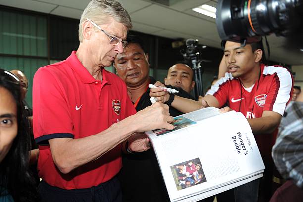 English Premier League team Arsenal manager Arsene Wenger autographs a book from Indonesian fan on arrival in Jakarta's Halim Perdanakusuma airport on July 12, 2013. The team arrived ahead of a friendly game with Indonesia Dream Team on July 14, 2013 as part of the Arsenal Asia Tour.   AFP PHOTO / ROMEO GACAD        