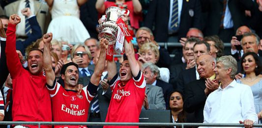 LONDON, ENGLAND - MAY 17: Captain Thomas Vermaelen of Arsenal (2R) lifts the trophy in celebration alongside Lukas Podolski (L), Mikel Arteta (2L) and Arsene Wenger manager of Arsenal (R) after the FA Cup with Budweiser Final match between Arsenal and Hull City at Wembley Stadium on May 17, 2014 in London, England. (Photo by Clive Mason/Getty Images)