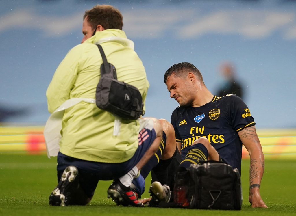 Arsenal's Swiss midfielder Granit Xhaka receives medical treatment before leaving the pitch injured during the English Premier League football match between Manchester City and Arsenal at the Etihad Stadium in Manchester, north west England, on June 17, 2020. - The Premier League makes its eagerly anticipated return today after 100 days in lockdown but behind closed doors due to coronavirus restrictions. (Photo by Dave Thompson / POOL / AFP) / RESTRICTED TO EDITORIAL USE. No use with unauthorized audio, video, data, fixture lists, club/league logos or 'live' services. Online in-match use limited to 120 images. An additional 40 images may be used in extra time. No video emulation. Social media in-match use limited to 120 images. An additional 40 images may be used in extra time. No use in betting publications, games or single club/league/player publications. /  (Photo by DAVE THOMPSON/POOL/AFP via Getty Images)