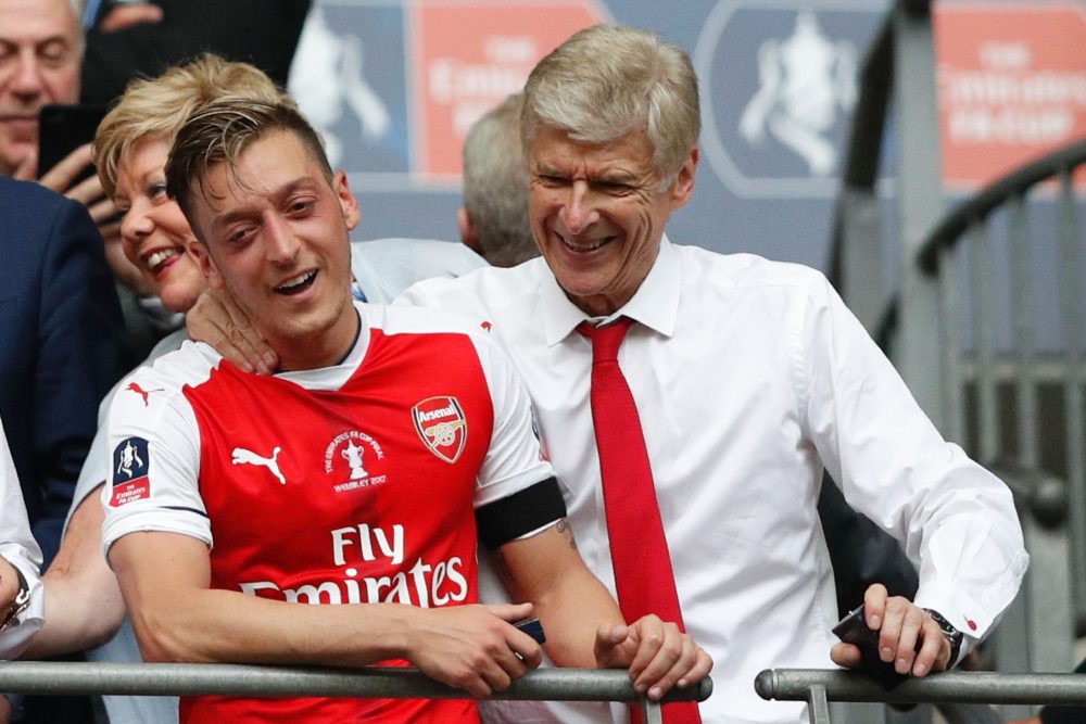 Arsenal's French manager Arsene Wenger (R) and Arsenal's German midfielder Mesut Ozil smile as Arsenal players celebrate their victory over Chelsea in the English FA Cup final football match between Arsenal and Chelsea at Wembley stadium in London on May 27, 2017. Aaron Ramsey scored a 79th-minute header to earn Arsenal a stunning 2-1 win over Double-chasing Chelsea on Saturday and deliver embattled manager Arsene Wenger a record seventh FA Cup. / AFP PHOTO / Adrian DENNIS