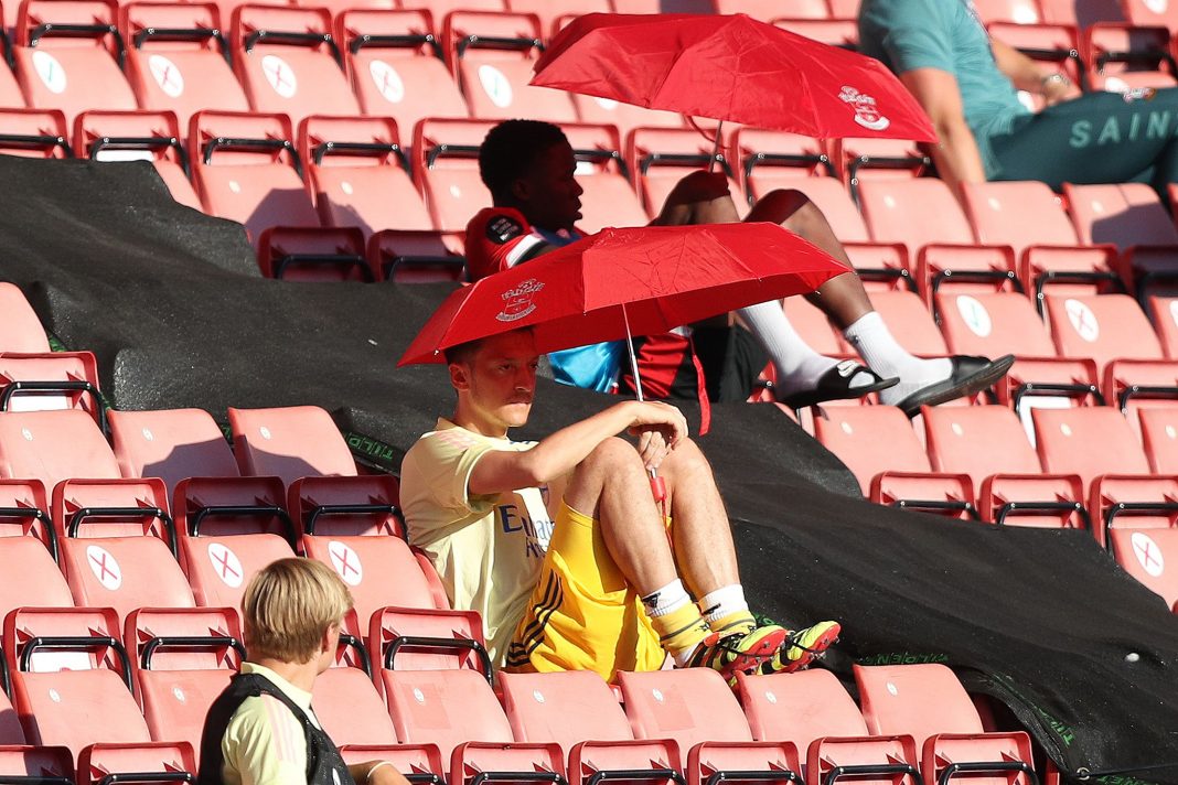 Arsenal's German midfielder Mesut Ozil (C) shelters from the sunshine beneath an umbrella during the English Premier League football match between Southampton and Arsenal at St Mary's Stadium in Southampton, southern England on June 25, 2020. (Photo by Andrew Matthews / POOL / AFP)