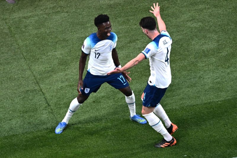 England's forward #17 Bukayo Saka (L) celebrates with his teammate midfielder #04 Declan Rice after scoring his team's second goal during the Qatar 2022 World Cup Group B football match between England and Iran at the Khalifa International Stadium in Doha on November 21, 2022. (Photo by JEWEL SAMAD/AFP via Getty Images)