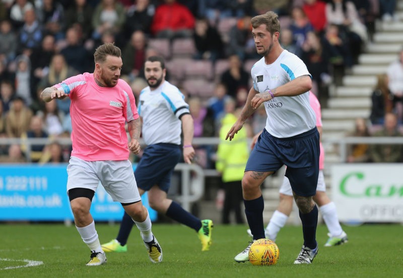 NORTHAMPTON, ENGLAND - APRIL 15: Reality Televison Personality Daniel Osborne moves forward with the ball watched by formerTottenham Hotspur footballer Jamie O'Hara during a Celebrity Charity Match at Sixfields on April 15, 2018 in Northampton, England. (Photo by Pete Norton/Getty Images)