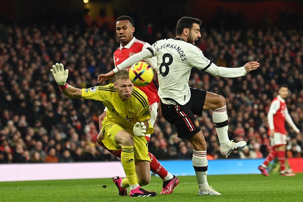 Manchester United's Portuguese midfielder Bruno Fernandes (R) just fails to get his shot on target as he collides with Arsenal's English goalkeeper Aaron Ramsdale (L) during the English Premier League football match between Arsenal and Manchester United at the Emirates Stadium in London on January 22, 2023. (Photo by GLYN KIRK/AFP via Getty Images)
