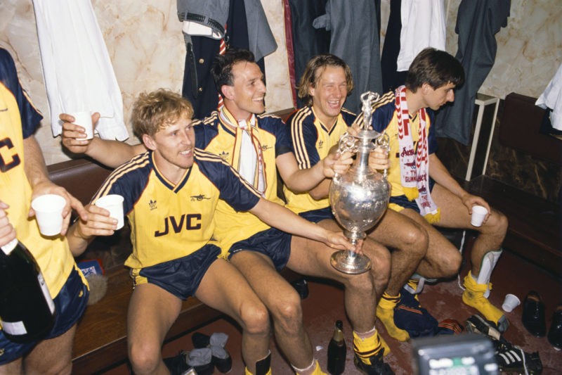 LIVERPOOL, UNITED KINGDOM - MAY 26:  Arsenal players from left Kevin Richardson, Steve Bould, Paul Merson and Alan Smith celebrate in the dressing room with the League Division One trophy after Arsenal had beaten Liverpool 2-0 in the final game of the season to pip Liverpool to the title, at Anfield on May 26, 1989 in Liverpool, England. (Photo by Allsport/Getty Images)