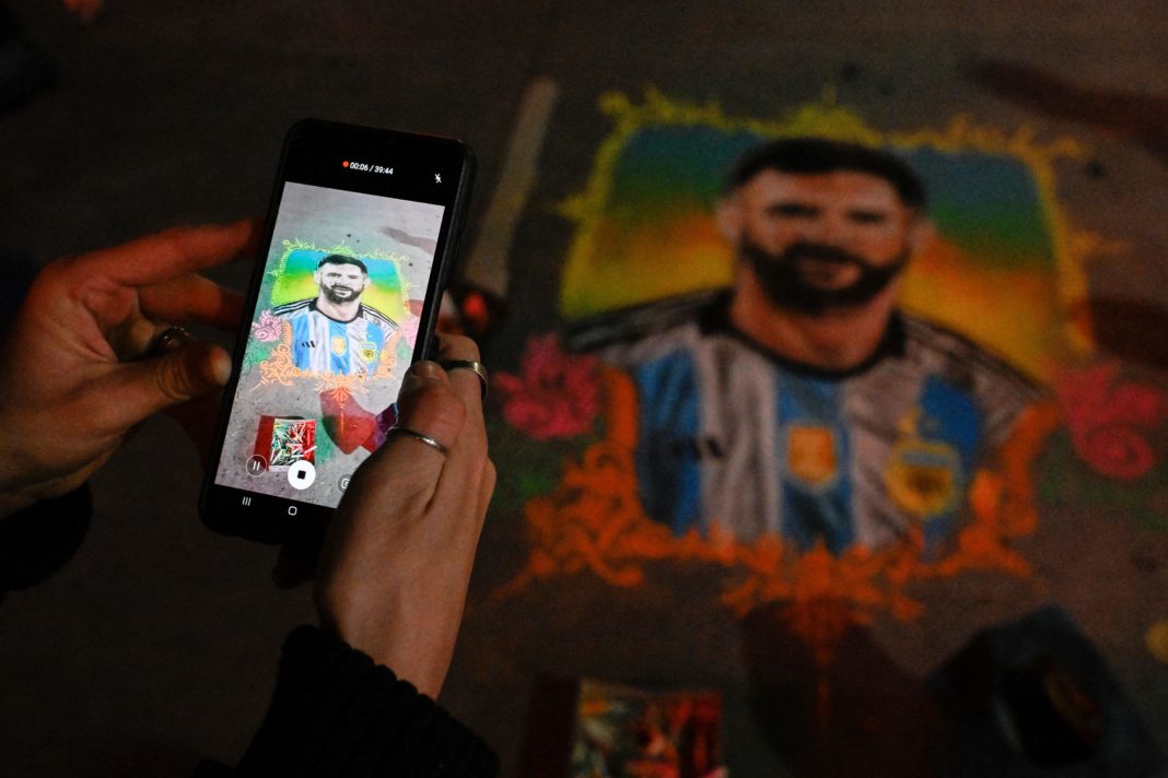 TOPSHOT - A woman takes a photo of a drawing by artist Claudio Pampillon depicting Argentine football star Lionel Messi, at the 9 de Julio avenue in Buenos Aires, on June 19, 2023. (Photo by LUIS ROBAYO / AFP) (Photo by LUIS ROBAYO/AFP via Getty Images)
