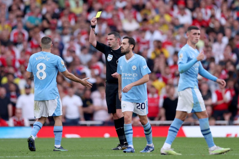LONDON, ENGLAND - OCTOBER 08: Match Referee Michael Oliver shows a yellow card to Mateo Kovacic of Manchester City during the Premier League match between Arsenal FC and Manchester City at Emirates Stadium on October 08, 2023 in London, England. (Photo by Alex Pantling/Getty Images)