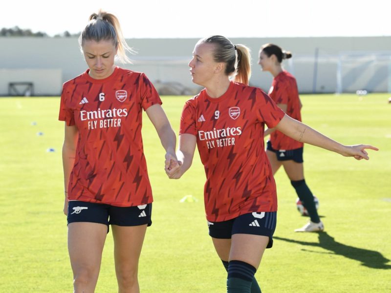 Arsenal in training with Emily Fox in the background [via Getty Images]