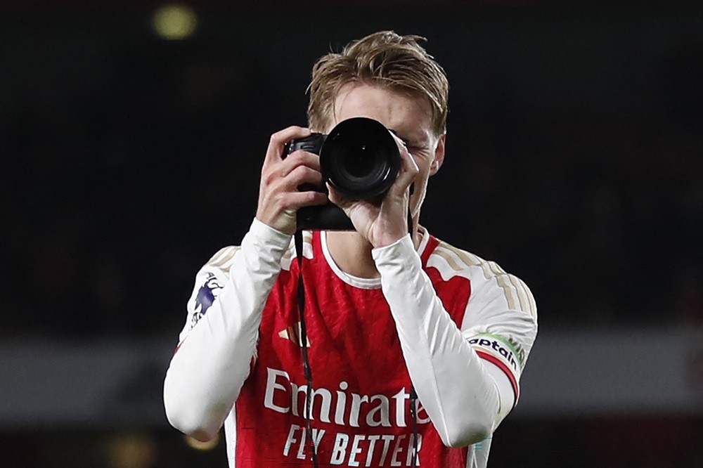 Arsenal's Martin Odegaard picks up a camera and takes pictures as he celebrates at the end of the English Premier League football match between Arsenal and Liverpool at the Emirates Stadium in London on February 4, 2024. (Photo by IAN KINGTON/IKIMAGES/AFP via Getty Images)