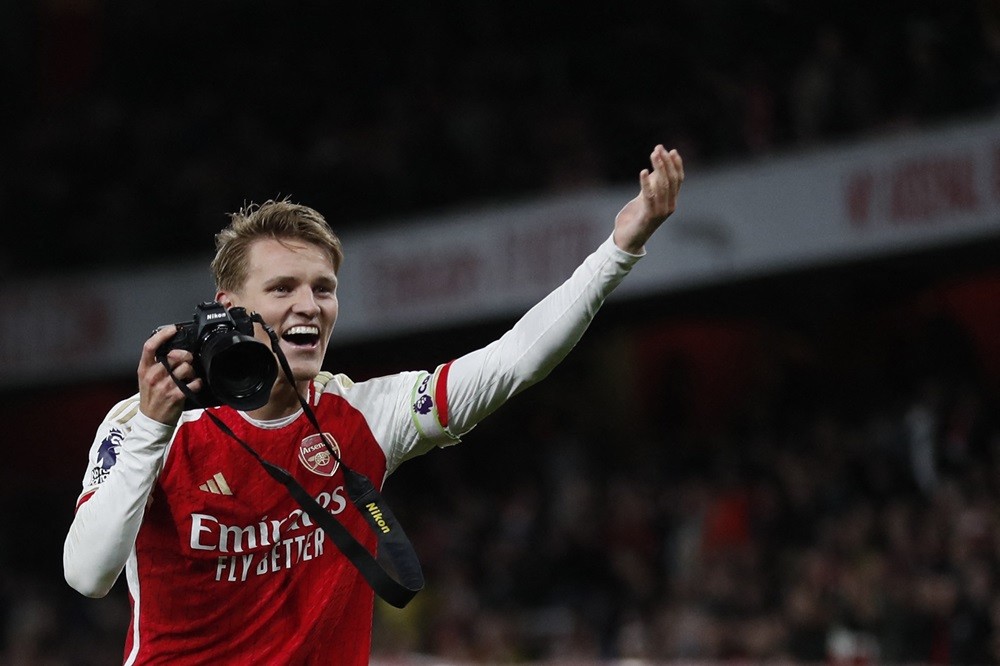 Arsenal's Martin Odegaard picks up a camera and takes pictures as he celebrates at the end of the English Premier League football match between Arsenal and Liverpool at the Emirates Stadium in London on February 4, 2024. (Photo by IAN KINGTON/IKIMAGES/AFP via Getty Images)