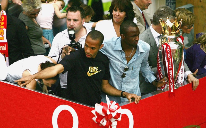 LONDON - MAY 16: Thierry Henry (L) and Patrick Vieira are seen at the front of the bus outside the Islington Town Hall during the Arsenal Football Club victory parade to show the League Champions with their FA Barclaycard Premiership Trophy on May 16, 2004 in Highbury, London. (Photo by Clive Mason/Getty Images)