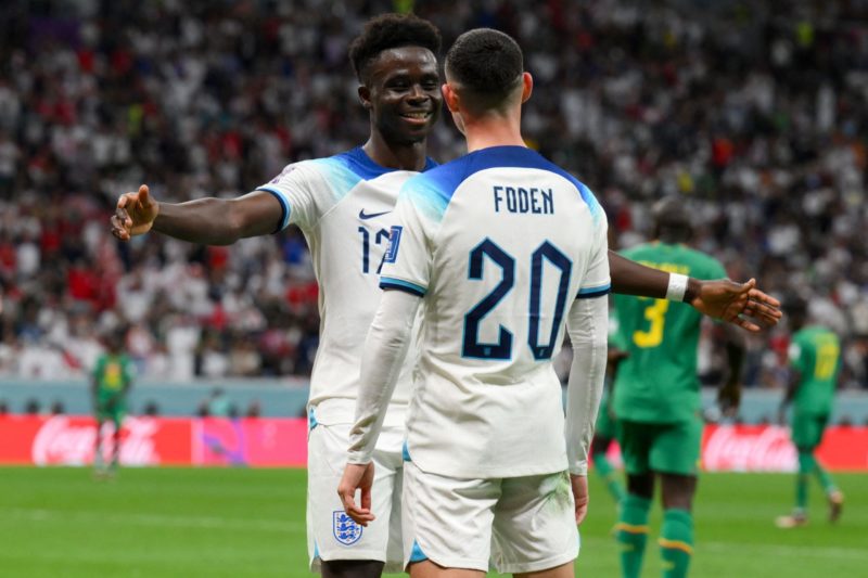 England's forward #17 Bukayo Saka celebrates with England's forward #20 Phil Foden after scoring his team's third goal during the Qatar 2022 World Cup round of 16 football match between England and Senegal at the Al-Bayt Stadium in Al Khor, north of Doha on December 4, 2022.(Photo by PAUL ELLIS/AFP via Getty Images)
